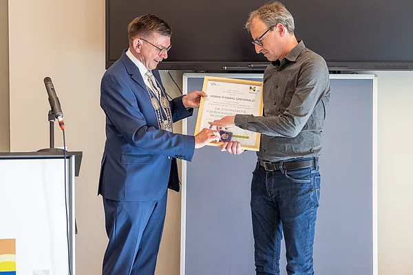 Erster Bürgermeister Armin Warmuth überreicht Herrn Dr. Thomas Greinwald die Stadtplakette und eine Urkunde.
